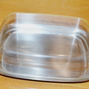 May include: A silver butter dish with a clear glass lid. The dish is oval shaped and has a smooth, shiny surface.