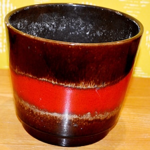 May include: A brown and red ceramic planter with a wide rim and a glazed finish. The planter has a red band around the middle.
