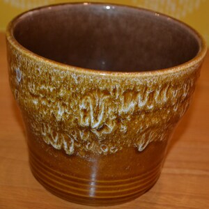 May include: A brown ceramic planter with a white glaze pattern. The planter has a wide rim and a rounded bottom.
