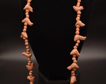 May include: A long necklace featuring light brown, matte-finish beads interspersed with carved bird-shaped charms. The necklace consists of a repeating pattern of small round beads and larger, detailed bird figures, all in a uniform earthy clay tone.