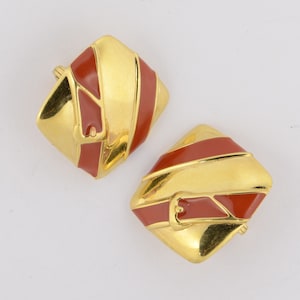 May include: A pair of gold-tone earrings with red enamel accents. The earrings are shaped like squares with rounded corners and have a diagonal stripe design.