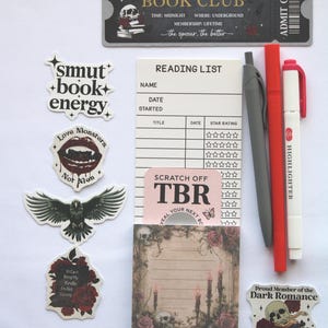 Op de afbeelding: Een verzameling briefpapier en stickers met een donker romantisch thema. Bevat een ticket, leeslijst, notitieblok, pennen en stickers met zinnen als "smut + book + energy" en "Love Monsters".