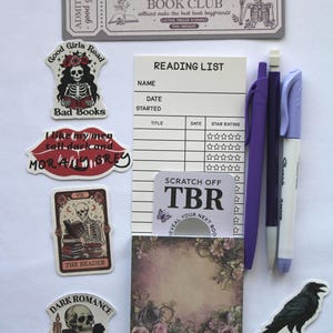 Op de afbeelding: Een verzameling briefpapierartikelen met een donker romantisch thema. Inclusief stickers met skelet- en ravenillustraties, een leeslijstnotitieblok, pennen en een kras-TBR-kaart. Het kleurenpalet is voornamelijk zwart, wit en paars.