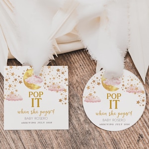 May include: Two baby shower favor tags with a moon, clouds, and stars design. The text on the tags reads "Pop It When She Pops! Baby Rosero Arriving July 2023".