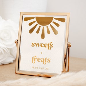 May include: Gold framed sign with a gold sun graphic and the text "sweets + treats" and "Please take one".