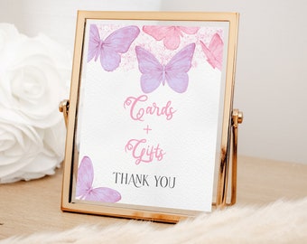 May include: A framed sign with a gold metal frame. The sign has a white background with watercolor butterflies in shades of pink and purple. The text reads "Cards + Gifts THANK YOU".