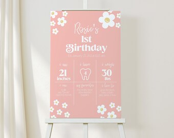 May include: A pink and white first birthday sign with a daisy pattern. The sign says "Rosie's 1st Birthday" and includes details about the child's height, weight, and favorite foods.