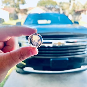 May include: A clear glass button with the words "Engine Start Stop" engraved on it. The button is being held in front of a black car.