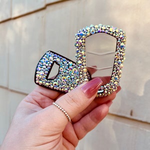 May include: Two key fobs covered in iridescent rhinestones. The key fobs are silver and black.