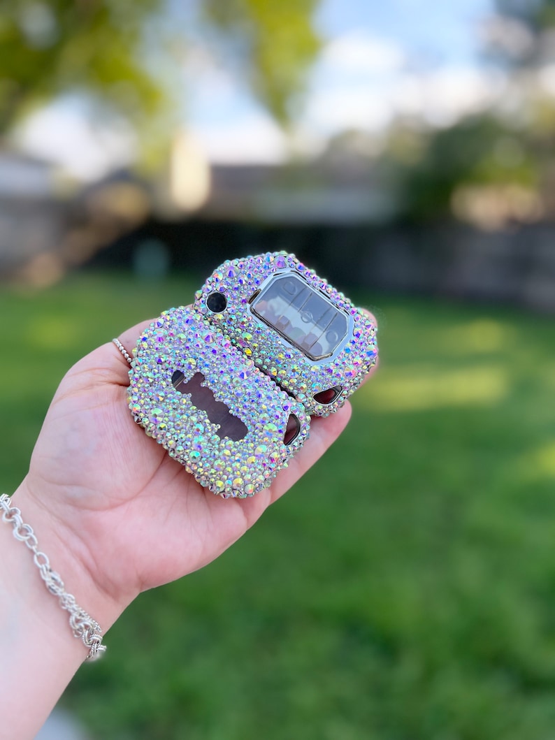 Pu&ograve; includere: Una custodia per telecomando per chiavi auto aperta, tempestata di strass iridescenti. La custodia della chiave mostra i pulsanti della chiave e la chiave stessa. Gli strass sono un mix di colori, tra cui rosa, giallo e blu.