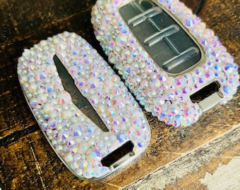 May include: Two car key covers with a clear plastic base and a design of iridescent rhinestones. The covers are in the shape of a car key fob.