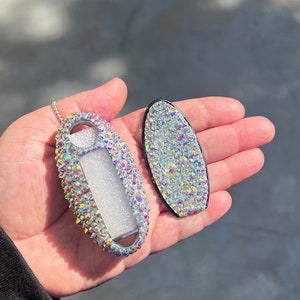 Pu&ograve; includere: Un portachiavi e una copertura per chiavi ricoperti di cristalli iridescenti. Il portachiavi ha una catena d'argento e una finestra trasparente. La copertura della chiave &egrave; di forma ovale con un bordo nero. Entrambi gli articoli sono ricoperti di cristalli scintillanti.
