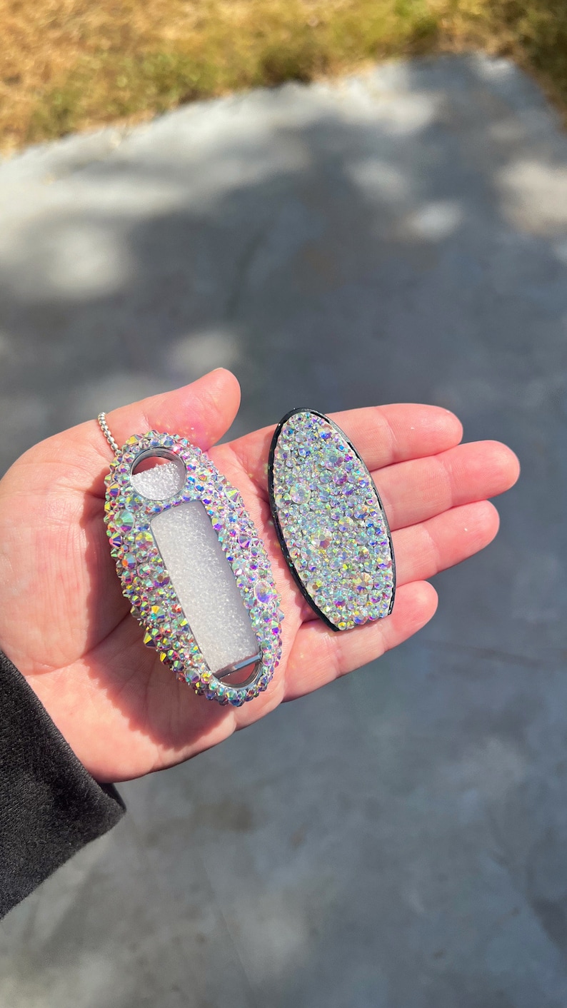 Pu&ograve; includere: Un portachiavi e una copertura per chiavi ricoperti di cristalli iridescenti. Il portachiavi ha una catena d'argento e una finestra trasparente. La copertura della chiave &egrave; di forma ovale con un bordo nero. Entrambi gli articoli sono ricoperti di cristalli scintillanti.
