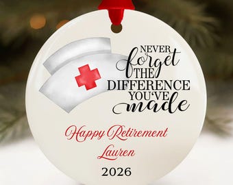 May include: A white ceramic ornament with a red ribbon for hanging. The ornament features a nurse's cap with a red cross and the text "Never forget the difference you've made." It also includes "Happy Retirement Lauren 2026" in red.