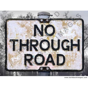 May include: Weathered rectangular road sign with the words "NO THROUGH ROAD" in black lettering. The sign has a white background with peeling paint and a dark border. A metal cap is at the top.