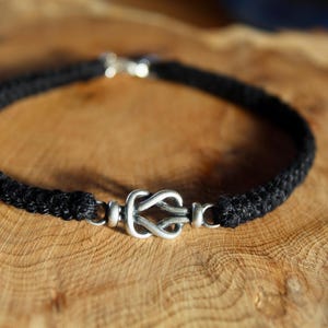 May include: A black braided cord bracelet with a silver knot clasp.