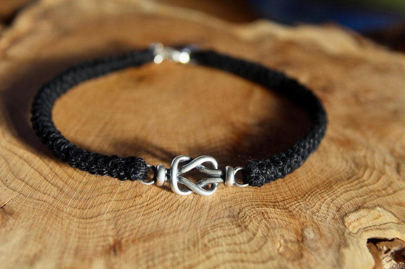 May include: A black braided cord bracelet with a silver knot clasp.
