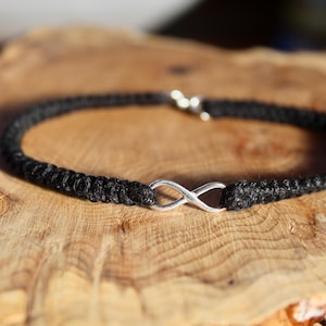 May include: A black braided cord bracelet with a silver infinity symbol charm.