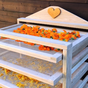 Peut inclure: Un séchoir en bois à cinq étages pour sécher les herbes et les fleurs. L'étagère supérieure a une découpe en forme de cœur et est remplie de fleurs de calendula orange.