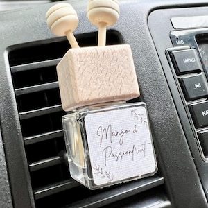May include: A car air freshener with a wooden base and two wooden sticks. The bottle is clear and contains a liquid. The label on the bottle says "Mango & Passionfruit".