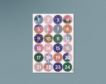 Pode incluir: Uma folha de 24 adesivos redondos coloridos com os números de 1 a 24. Cada adesivo tem um padrão diferente.