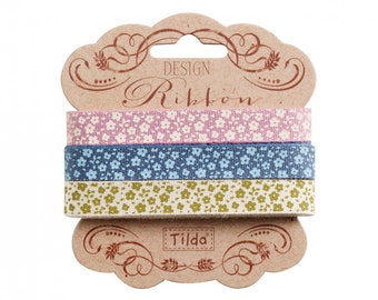 May include: Three floral patterned ribbons in pink, blue, and green, presented on a brown card. The card features the words "DESIGN Ribbon" and the brand name "Tilda". These fabric ribbons are ideal for crafting and decorative purposes.