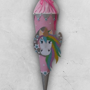 Könnte beinhalten: Ein rosa-silberner Schultüte mit einem Einhorn-Motiv. Das Einhorn hat eine Regenbogenmähne und ein goldenes Horn. Die Tüte ist mit Sternen und Glitzer verziert.
