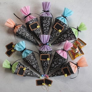 Könnte beinhalten: Eine Sammlung von zehn schwarzen und weißen kegelförmigen Partytaschen mit Kreidetafel-Etiketten. Die Taschen sind mit buntem Seidenpapier gefüllt und mit schwarzem Band gebunden. Die Taschen sind in einem Kreis auf einer weißen Oberfläche angeordnet.