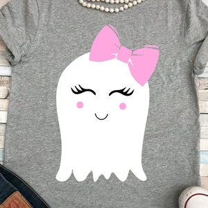 May include: A gray t-shirt with a white ghost wearing a pink bow. The ghost has eyelashes, rosy cheeks, and a smiling mouth.