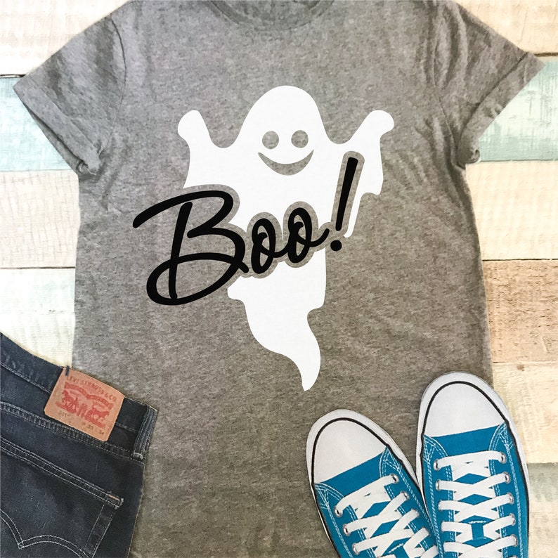 May include: A gray t-shirt with a white ghost and the text "Boo!" printed on it. The shirt is laying on a wooden surface with a pair of blue sneakers next to it.
