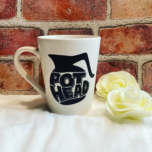 May include: White ceramic coffee mug with a black graphic of a coffee pot and the text "POT HEAD".