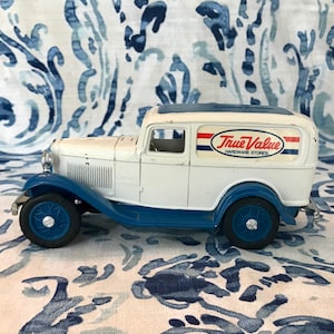May include: A white and blue vintage True Value Hardware Stores delivery truck toy. The toy truck has blue wheels and trim, with the True Value logo on the side. The toy is a classic collectible.