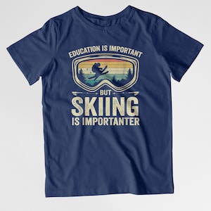 May include: Navy blue t-shirt with a vintage-style graphic of a skier wearing goggles. The text reads "Education is important, but skiing is importanter."