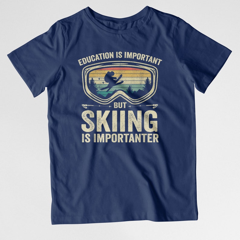 May include: Navy blue t-shirt with a vintage-style graphic of a skier wearing goggles. The text reads "Education is important, but skiing is importanter."