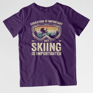 May include: Purple t-shirt with a vintage-style graphic of a skier wearing goggles. The text reads "Education is important, but skiing is importanter."