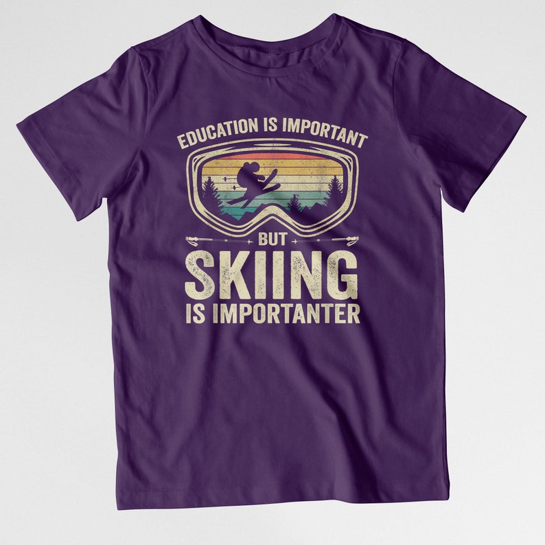 May include: Purple t-shirt with a vintage-style graphic of a skier wearing goggles. The text reads "Education is important, but skiing is importanter."