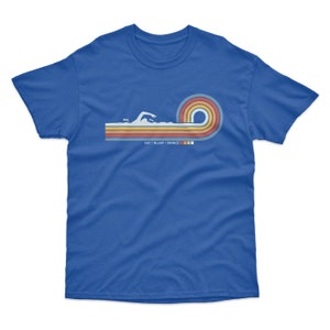 May include: A royal blue t-shirt with a retro-style graphic of a swimmer in a wave. The graphic is in shades of orange, yellow, and blue. The text "EAT - SLEEP - SWIM" is printed below the graphic.