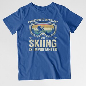 May include: Blue t-shirt with a vintage-style graphic of a skier wearing goggles. The text reads "Education is important, but skiing is importanter."