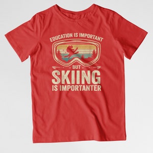 May include: Red t-shirt with a vintage-style graphic of a skier wearing goggles. The text reads "Education is important, but skiing is importanter."
