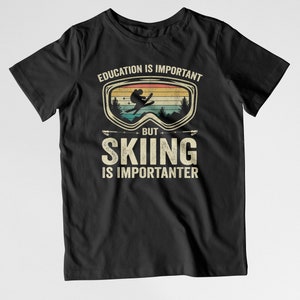 May include: Black t-shirt with a vintage-style graphic that says "Education is important, but skiing is importanter". The graphic features a skier in a pair of goggles against a sunset background.