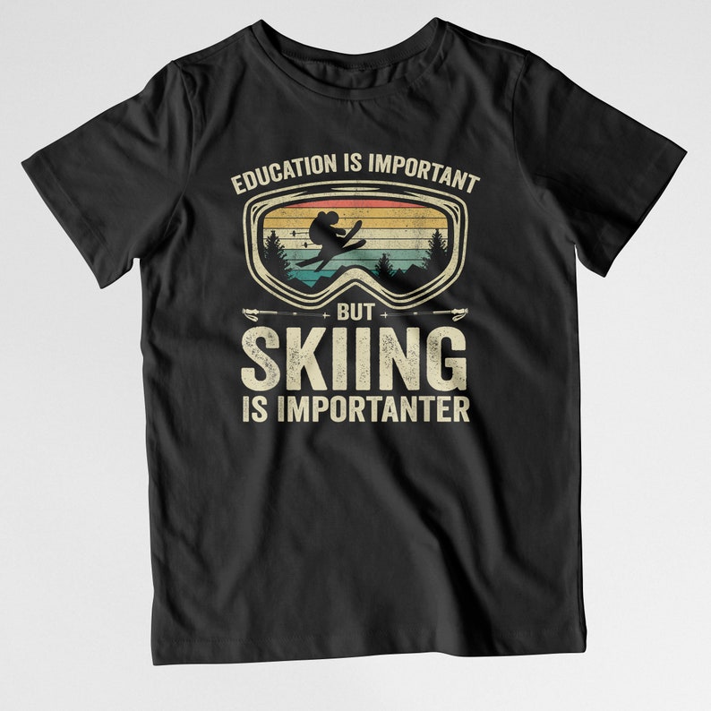 May include: Black t-shirt with a vintage-style graphic that says "Education is important, but skiing is importanter". The graphic features a skier in a pair of goggles against a sunset background.