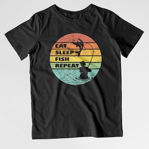 May include: Black t-shirt featuring a vintage-style graphic of a fisherman holding a fishing rod with a fish leaping out of the water. The graphic has a sunset background with the text "Eat Sleep Fish Repeat".