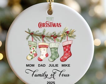 May include: A white ceramic Christmas ornament with a gold string. The ornament features the words "Merry Christmas" and four hanging stockings. The names "Mom Dad Julie Mike" and "Family of Four 2025" are also printed on the ornament.