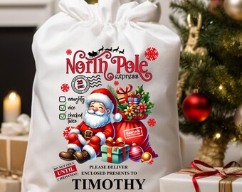 May include: White drawstring gift bag with a festive Santa Claus design. The bag features the text "North Pole Express" and "Please deliver enclosed presents to Timothy". A red sack of gifts and Christmas ornaments are also shown.