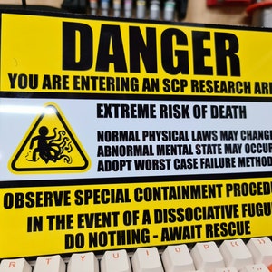 May include: A yellow and black warning sign with the text "DANGER" and "YOU ARE ENTERING AN SCP RESEARCH AREA". The sign also includes a black and white illustration of a person with tentacles.