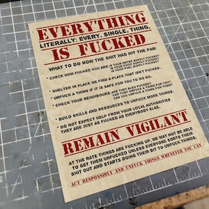 May include: A printed paper with the text "EVERYTHING IS FUCKED" in red and black. The paper includes a list of instructions and the phrase "REMAIN VIGILANT". The background is a grey cutting mat.