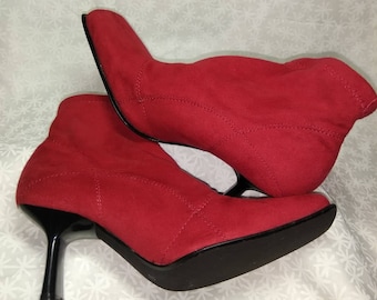 May include: A pair of red suede ankle boots with black heels. The boots have a pointed toe and a zipper on the back.