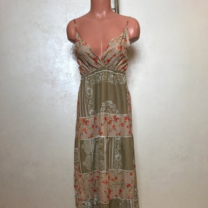 May include: A long, sleeveless maxi dress with a patchwork design. The dress is made of a light brown fabric with a white and red floral pattern. The dress has a V-neckline and a fitted bodice. The skirt is flowy and has a tiered design.