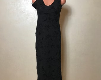 May include: A black maxi dress with a floral pattern. The dress has a V-neckline and thin straps. The dress is made of a sheer fabric with a velvet overlay.