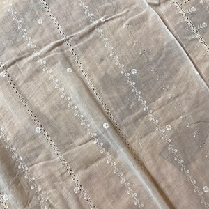 May include: White cotton fabric with a delicate embroidered pattern of small flowers and vines. The fabric has a sheer, lightweight texture and is perfect for crafting or sewing projects.